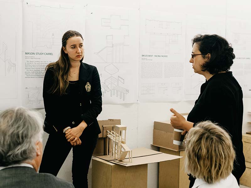Guest juror gives student feedback during a final review presentation in the Architecture West third floor atrium.