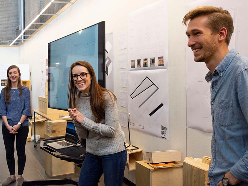 Three students present a project on a monitor in the Hinman Research Building