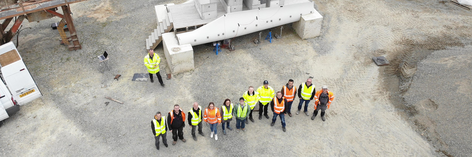 Aerial shot showing members of the Re-Wind Network stand in front of a pedestrian bridge made using decommissioned wind turbine blades
